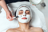 Cosmetologist applying the alginates facial mask to woman while lying on a stretcher in the spa center.