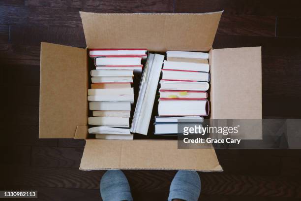 woman stands next to box of books - entrümpeln stock-fotos und bilder
