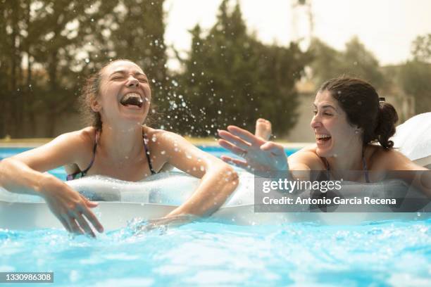two beautiful mid adult women enjoying a summer day in the pool on an inflatable mat - freibad stock-fotos und bilder