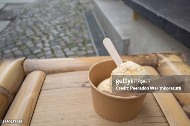 cup of scoop soy based umami ice-cream on bamboo chair on sidewalk outside store in berlin, germany. - whip cream dollop stock pictures, royalty-free photos & images