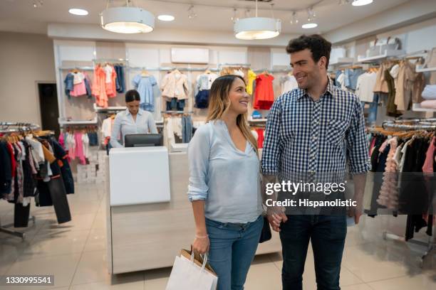 pregnant couple looking happy shopping for the baby at a clothing store - baby boutique stock pictures, royalty-free photos & images