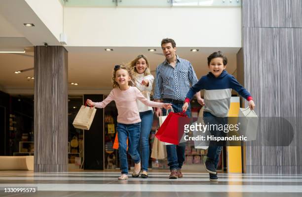 excited family shopping and kids running at the mall holding bags - family mall stockfoto's en -beelden