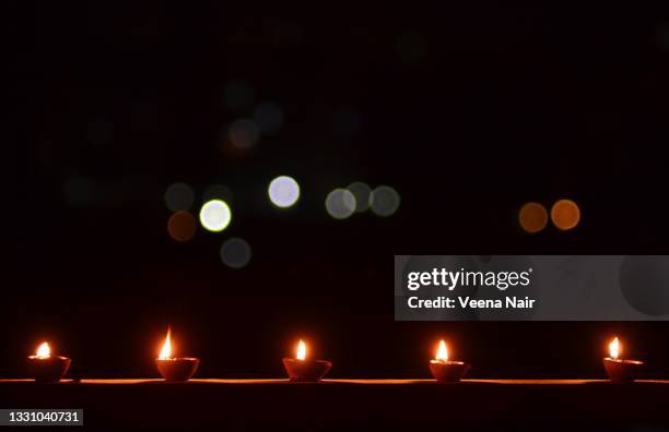 lit clay diya in a row on balcony with bokeh/diwali/copy space - diya oil lamp stock pictures, royalty-free photos & images