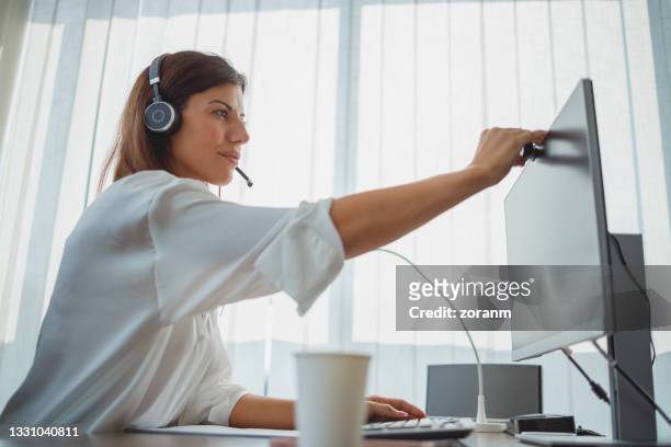 businesswoman sitting in her office with headset on and turning on webcam for video conference - slå på och av bildbanksfoton och bilder