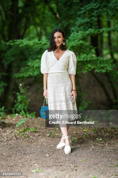 Guest wears a black and silver large pendant earring, a white with embroidered pattern V-neck and puffy sleeves t-shirt, a white cut-out midi skirt,...