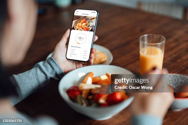 young woman using mobile app to track nutrition and count calories with smartphone - smartphone table stockfoto's en -beelden