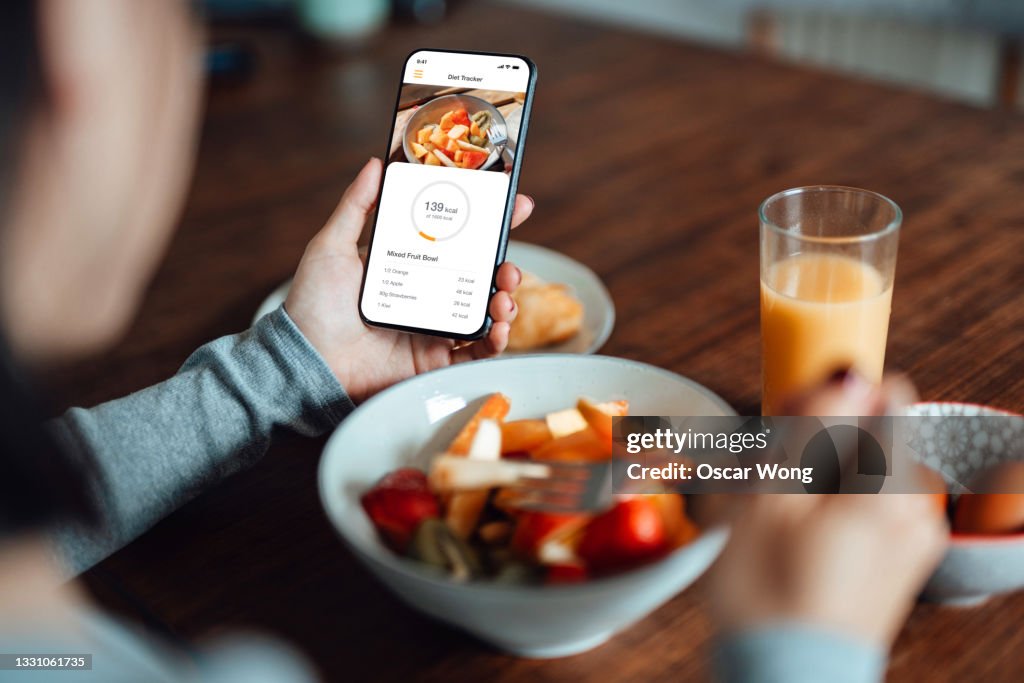 Young woman using mobile app to track nutrition and count calories with smartphone