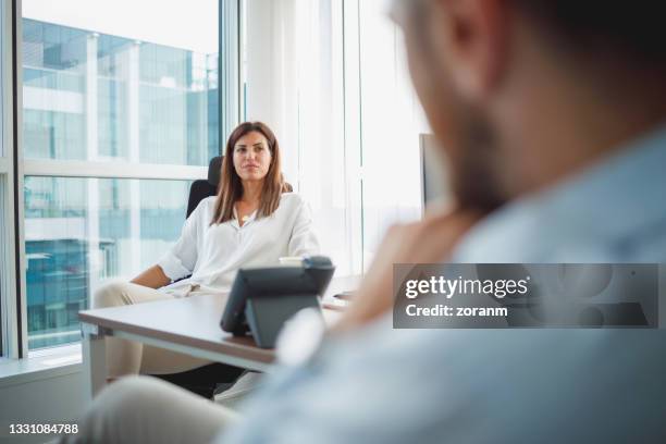 businesswoman sitting in her office and looking at candidate on job interview skeptically - suspicion employee stock pictures, royalty-free photos & images