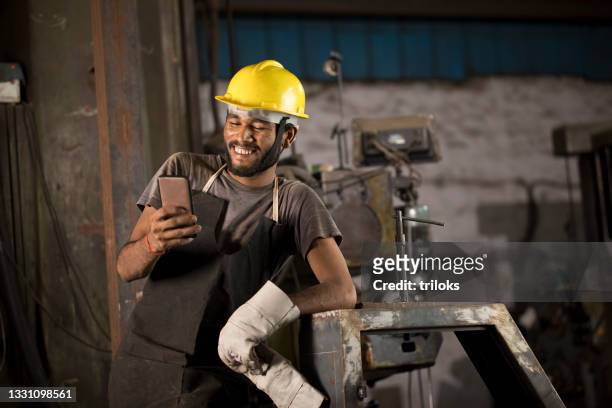 industriearbeiter in schutzkleidung sms auf dem handy - india phone professional stock-fotos und bilder