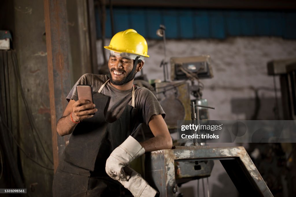 Industrial worker in protective workwear texting on mobile phone