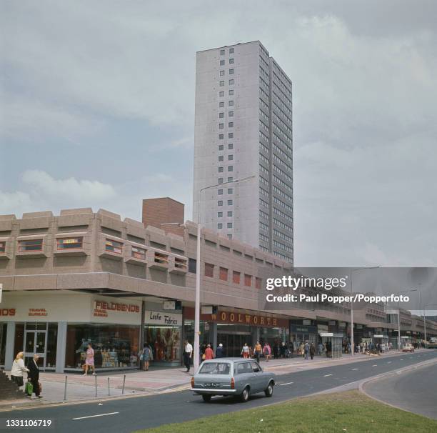 Car drives down Hankinson way past pedestrians visiting the new Salford Shopping Centre Precinct in the Pendleton area of the city of Salford near...