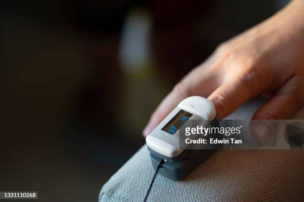 nahaufnahme des fingers einer asiatischen chinesischen mittelerwachsenen frau, der mit einem oximeter zur messung der sauerstoffsättigung im blut und der herzschlagrate zu hause befestigt ist covid-19-gesundheitstechnologie - medical technology stock-fotos und bilder