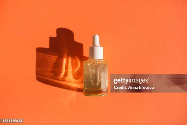 glass bottle with cosmetic liquid on bright orange background with shadow and light reflections. flat lay style and close-up. copy space for your design - enzymes cosmetics stockfoto's en -beelden