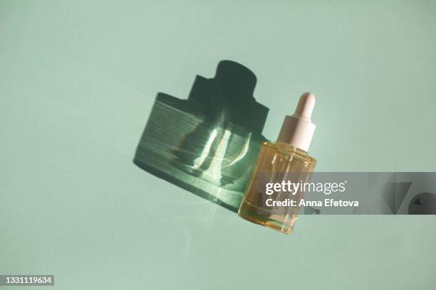 glass bottle with cosmetic liquid on pastel mint green background with shadow and light reflections. flat lay style and close-up. copy space for your design - enzymes cosmetics stockfoto's en -beelden