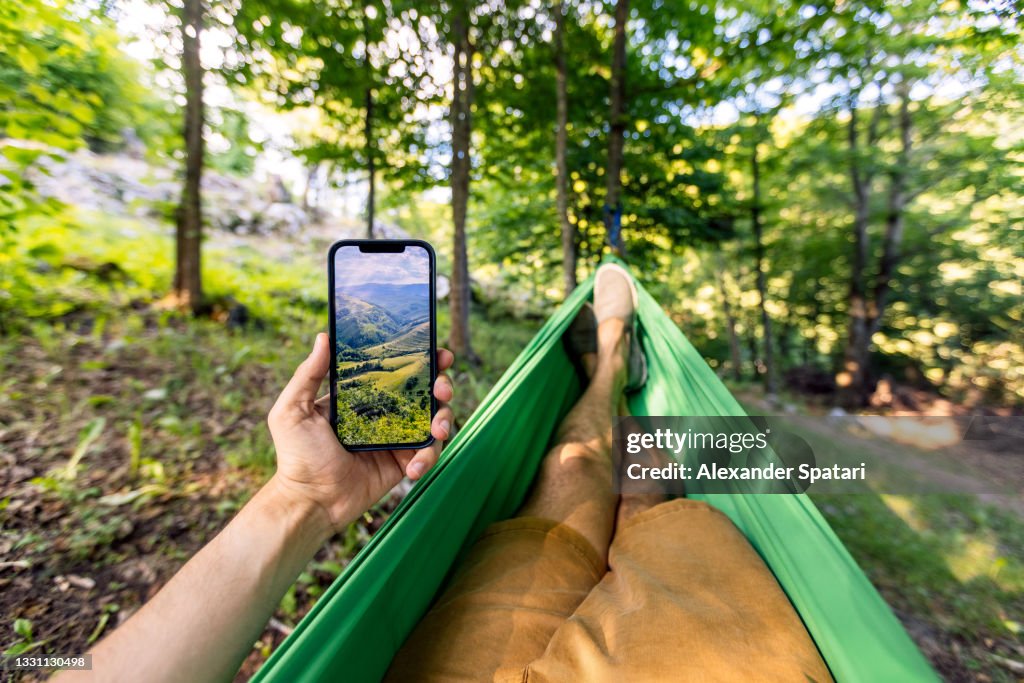 Man relaxing in the hammock and using smartphone, personal perspective POV
