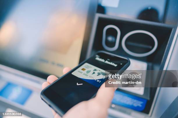 mann am geldautomaten mit smartphone geld abheben - financial technology stock-fotos und bilder