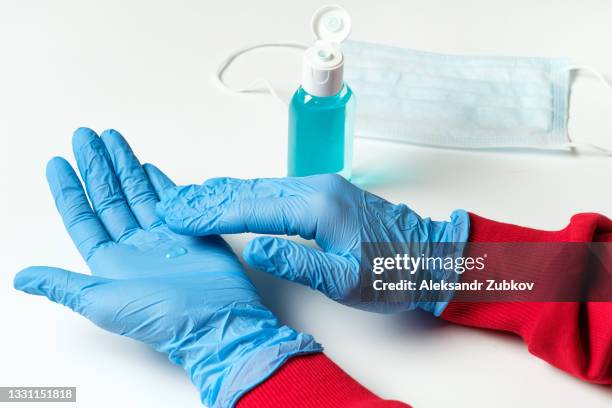 a nurse, a doctor, a medical worker, a woman in medical gloves applies an alcohol antiseptic on her hands, rubs it on the palm. next to it is a tube of disinfectant, a disposable mask. preventing the spread of viruses, infections, bacteria and coronavirus - blauer handschuh stock-fotos und bilder