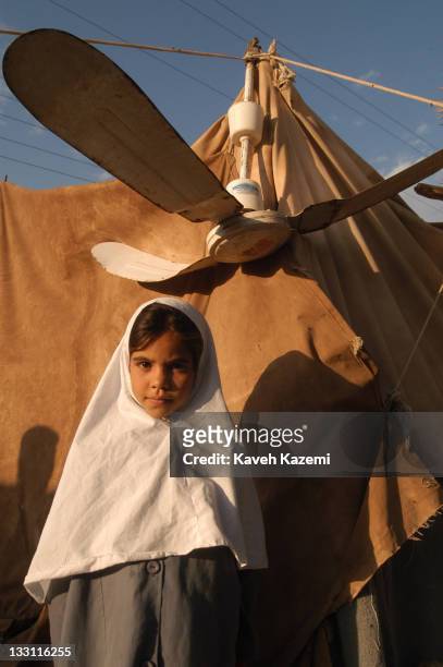 Young girl in a veil and school uniform who lost her home after the earthquake struck the city stands outside the tent where she lives with her...