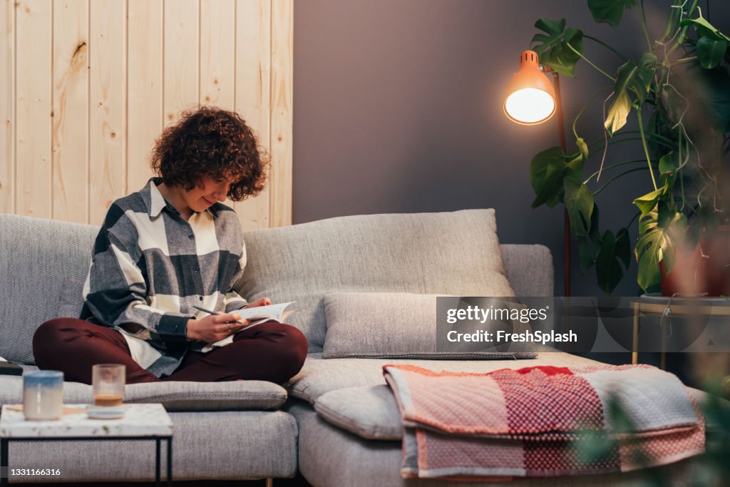 Smiling Young Woman Sitting on the Couch in her Living Room and Writing a Journal