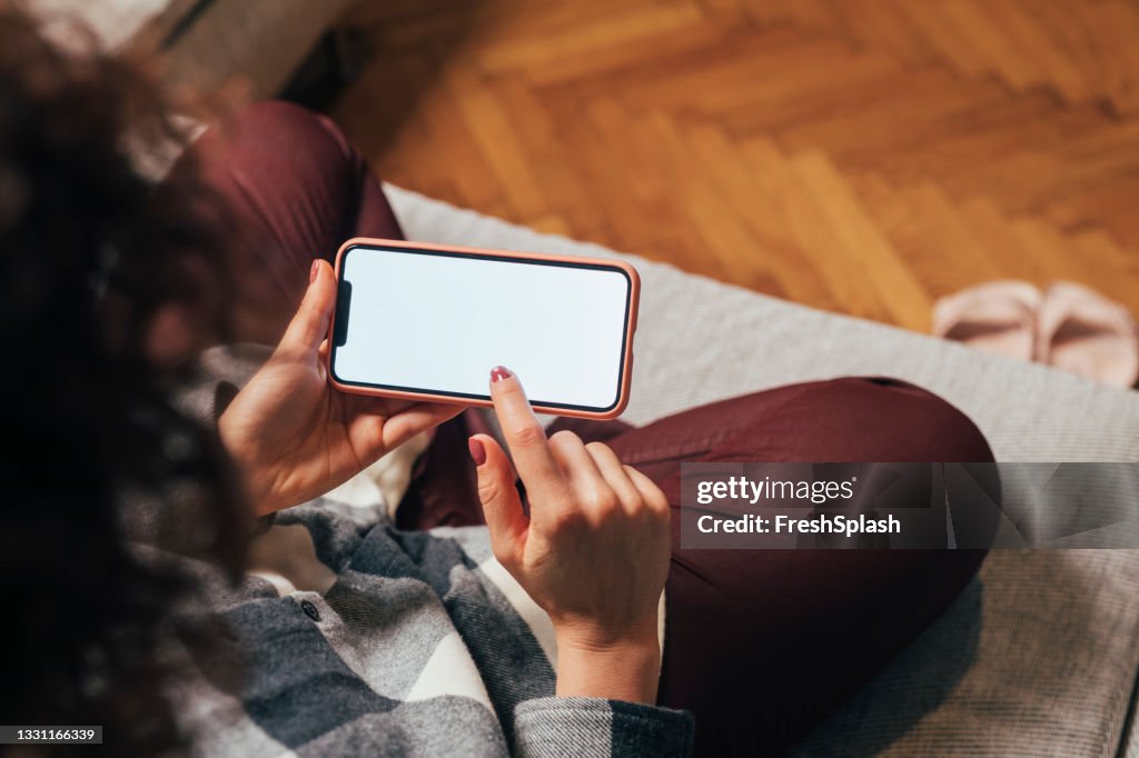 Schermo dello smartphone vuoto tenuto da una donna irriconoscibile seduta sul divano