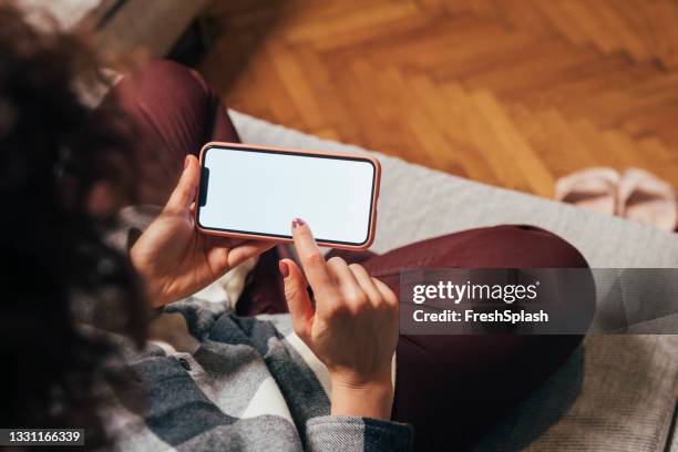 empty smartphone screen held by an unrecognizable woman sitting on the sofa - horizontaal stockfoto's en -beelden