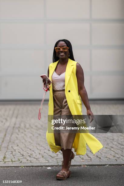 Lois Opoku wearing Bally sandals, beige Zara Culotte pants, Rodebjer shades and yellow Karl Lagerfeld coat on July 25, 2021 in Berlin, Germany.