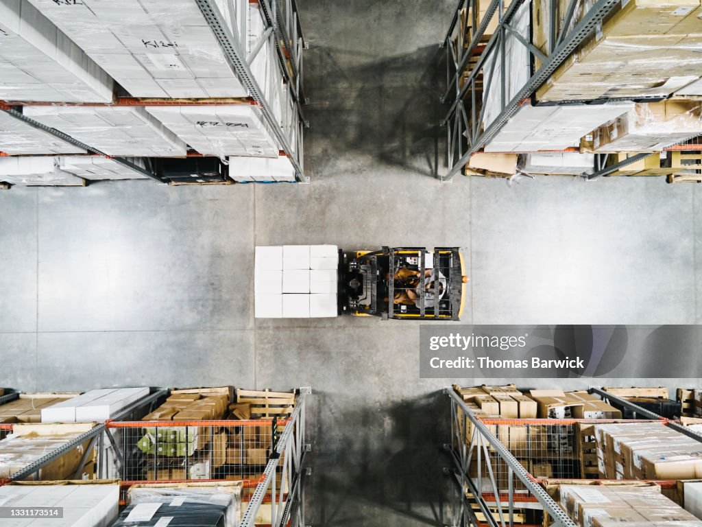 Overhead view of warehouse worker moving pallet of goods with forklift in warehouse