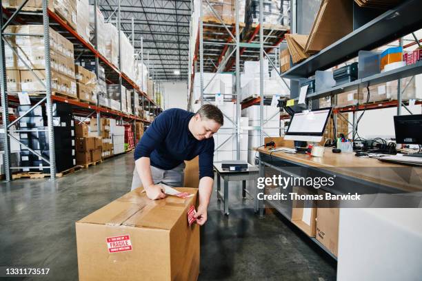 medium wide view of male warehouse worker labeling package with fragile stickers while shipping product from warehouse - shipping container top view - fotografias e filmes do acervo