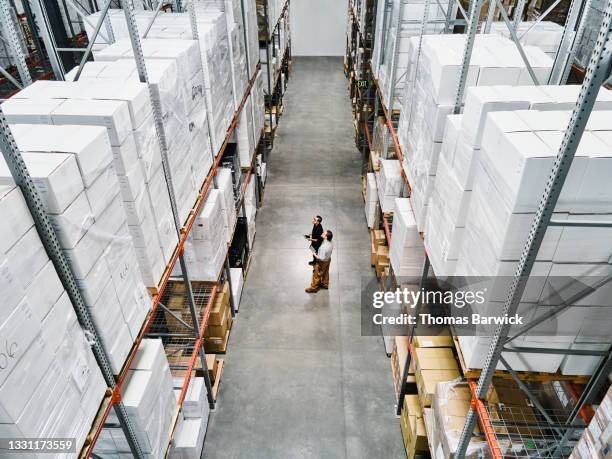 high angle view of warehouse employees in discussion while checking inventory with digital tablets - distribution warehouse technology stock pictures, royalty-free photos & images