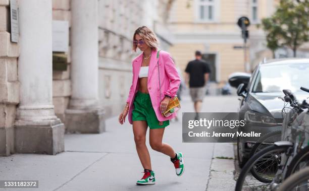 Karin Teigl wearing pink Arket blazer, white Dior bra, purple The Attico shades, green Prada shorts, colorful Chanel bag and green Nike sneakers on...