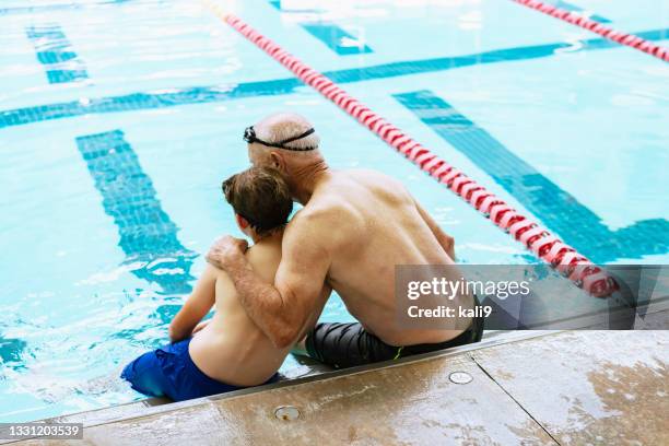großvater umarmt jungen, sitzt mit füßen im schwimmbad - sport bahnrunde stock-fotos und bilder