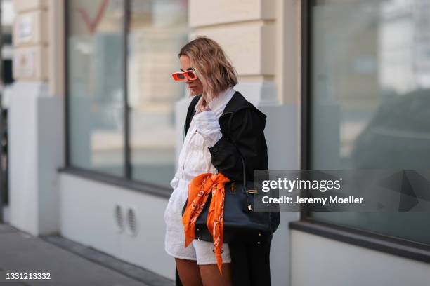 Karin Teigl wearing Prada nylon coat and white short, white and orange Loewe shades and black Hermes leather bag on July 20, 2021 in Munich, Germany.