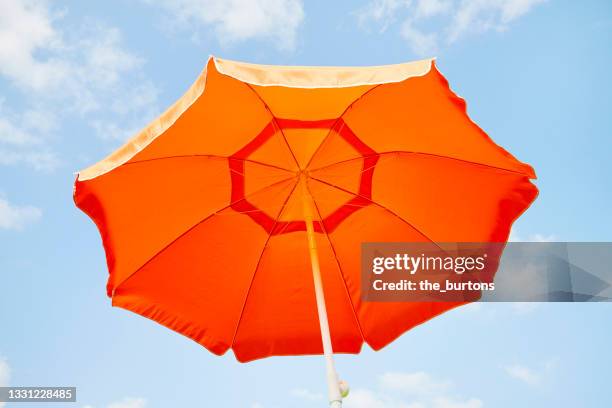 low angle view of orange parasol against blue sky and clouds - strandschirm stock-fotos und bilder