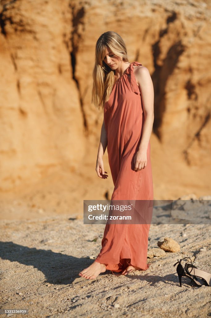 Beautiful woman in long sleeveless dress standing in the sun in stone desert