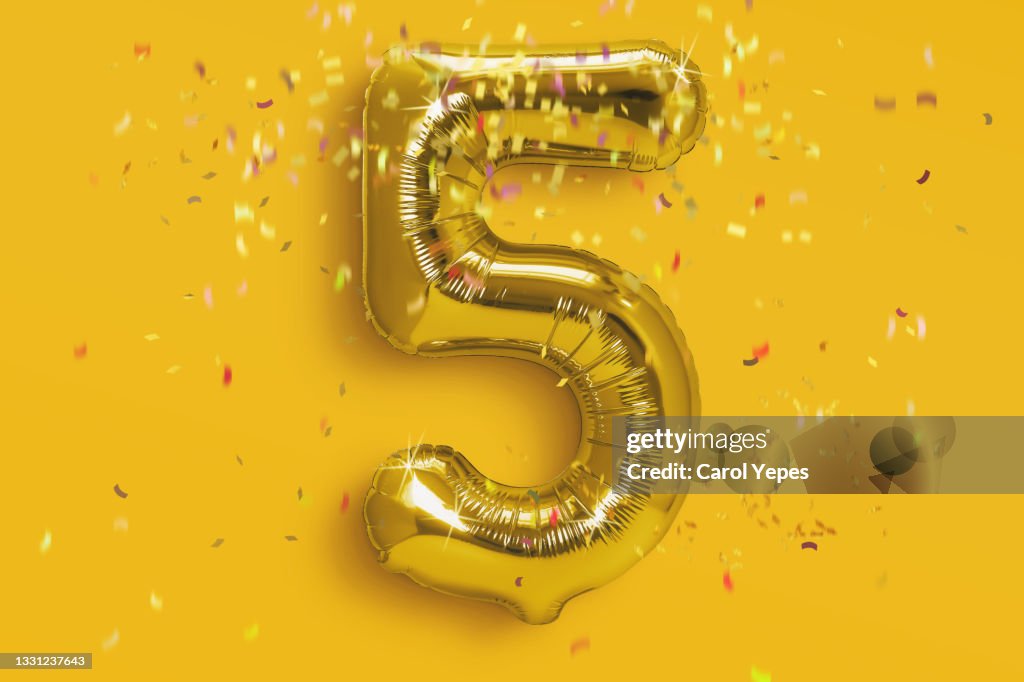Number 5 foil golden ballon in gold background with confetti