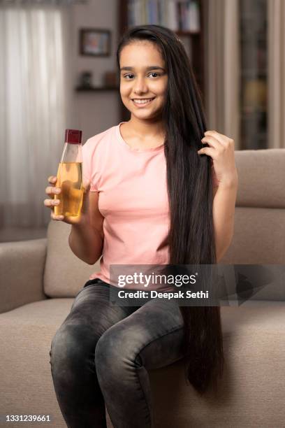 shot of a beautiful teenage girl showing hair oil bottle at home - girl long hair stock pictures, royalty-free photos & images