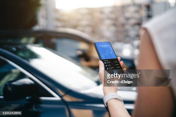 cropped shot of young woman managing online banking with mobile app on smartphone on the go, in front of her car in carpark. tracking and planning spending. transferring money, paying bills, checking account balance. smart banking with technology - car mobile stockfoto's en -beelden