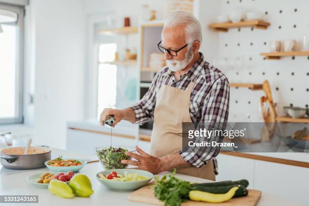 senior man making salad at kitchen counter - mediterranean diet stock pictures, royalty-free photos & images