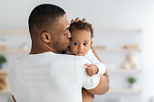Father's Care. Young Black Dad Holding And Kissing Adorable Newborn Baby