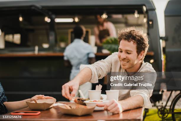 Young happy people eating at food truck outdoor - Focus on man face