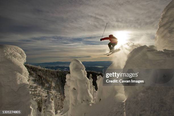 a skier launches off a jump over snowcoated trees. - whitefish montana stock pictures, royalty-free photos & images