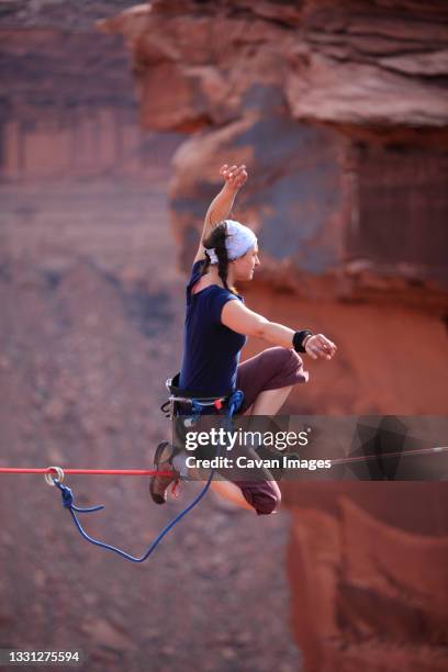 a female highliner poses on a highline at the fruit bowl in moab, utah, usa. - slackline stock-fotos und bilder