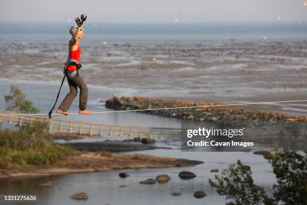 female slackliner walks a highline at longue-rive with the st. lawrence river in the background - highlining stock pictures, royalty-free photos & images