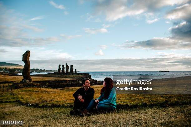 couple sitting on the grass of the ahu ko te riku in the tahat archaeological complex, easter island, chile - easter island fotografías e imágenes de stock