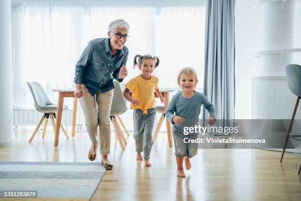 playful grandmother having fun while chasing her grandkids in the living room. - grandmas living room stockfoto's en -beelden