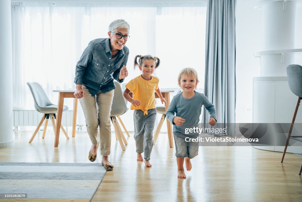 Playful grandmother having fun while chasing her grandkids in the living room.