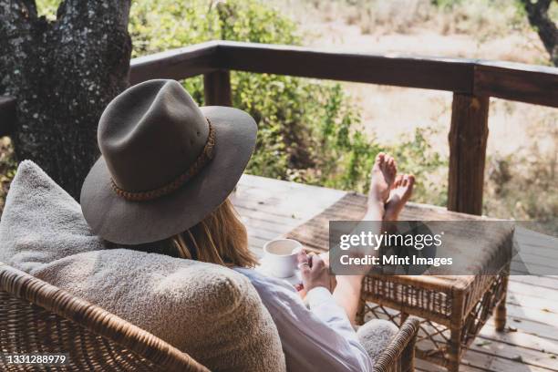 a woman sits with her feet up drinking a cup of tea, wearing a safari hat - クルーガー国立公園 ストックフォトと画像