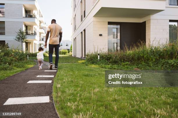 cute baby girl makes first steps at father's hand - stadswoning stockfoto's en -beelden