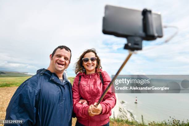 female taking selfie with disabled brother near english sea - beach shelter stockfoto's en -beelden
