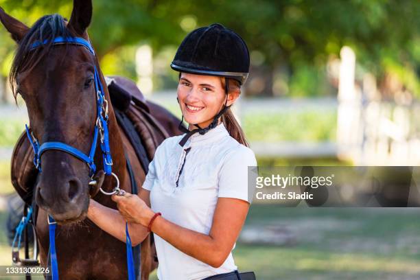 beautiful young woman in riding gear stroking her horse - cap hat stockfoto's en -beelden